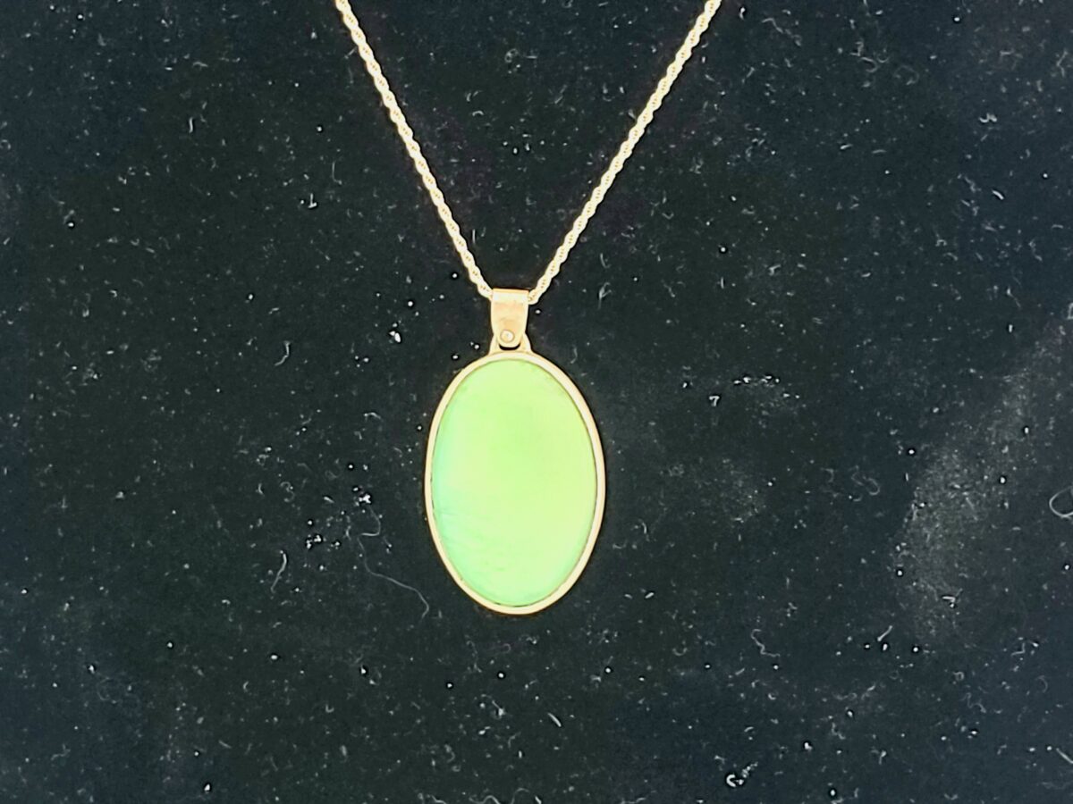image is of a simple sterling silver pendant with a mint green cab bezel set. The pendant is sitting on a black background.